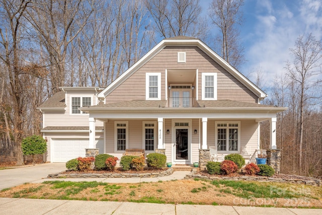 view of front facade with a porch, driveway, a shingled roof, and a garage