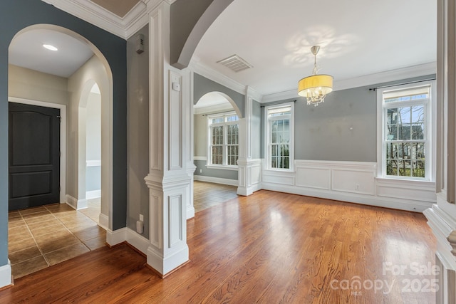 entrance foyer with a wainscoted wall, wood finished floors, visible vents, and crown molding