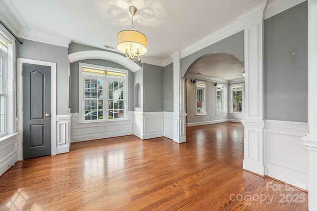 unfurnished room featuring arched walkways, wood finished floors, visible vents, ornamental molding, and ornate columns