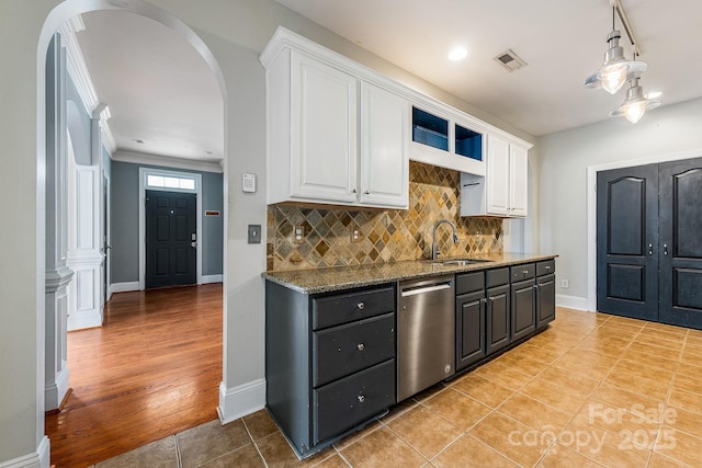 kitchen with a sink, white cabinetry, arched walkways, and dishwasher