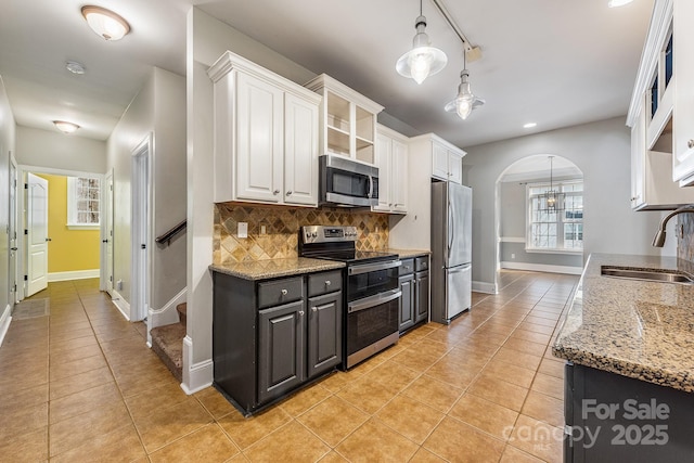 kitchen with arched walkways, light tile patterned floors, stainless steel appliances, white cabinetry, and a sink