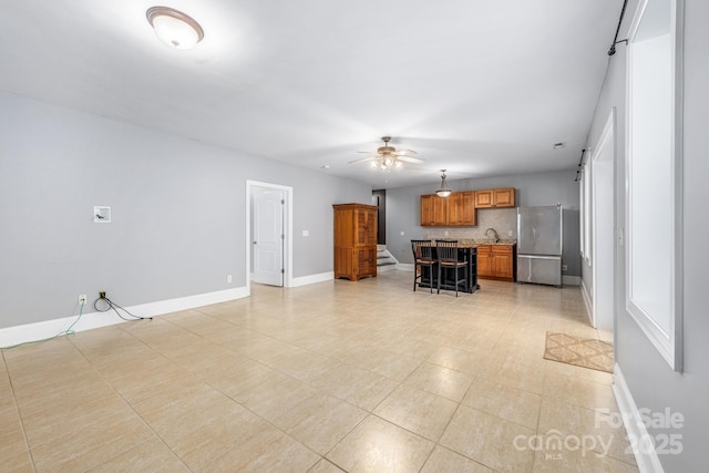 unfurnished living room featuring ceiling fan, a sink, and baseboards