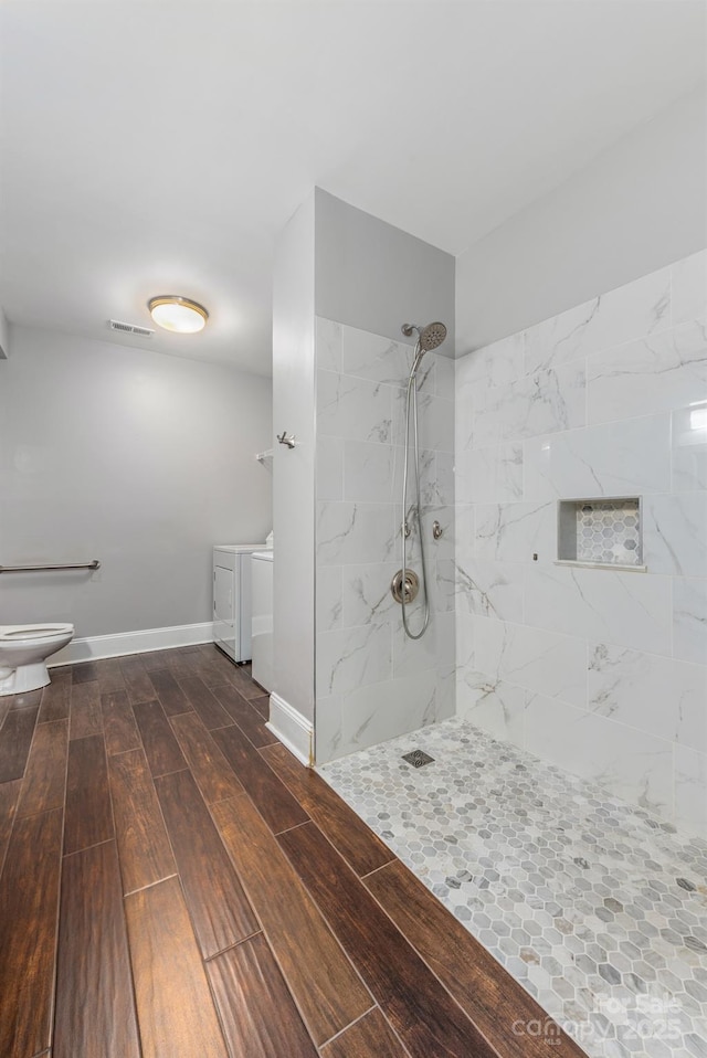 bathroom with baseboards, washer and clothes dryer, toilet, wood finished floors, and walk in shower