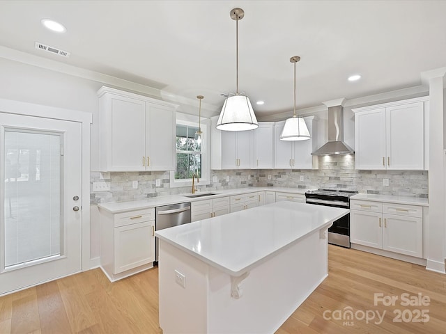 kitchen featuring visible vents, wall chimney range hood, appliances with stainless steel finishes, and white cabinetry