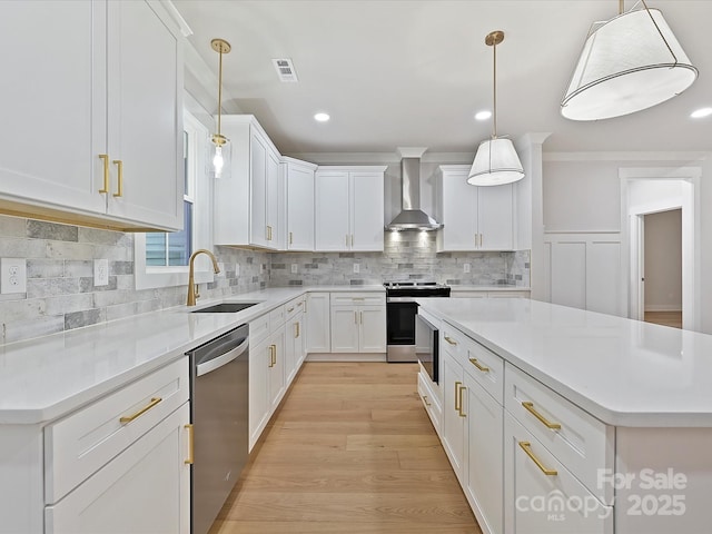 kitchen with wall chimney exhaust hood, stainless steel appliances, light countertops, white cabinetry, and a sink