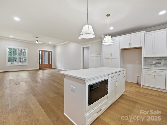 kitchen with light wood finished floors, white cabinetry, black microwave, and backsplash