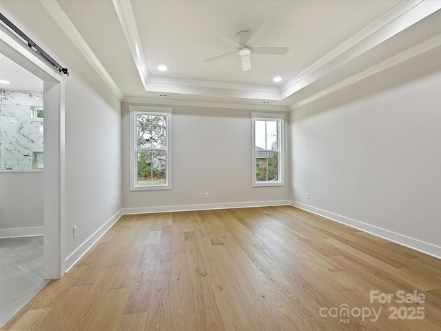 empty room with light wood finished floors, a barn door, ceiling fan, a tray ceiling, and crown molding