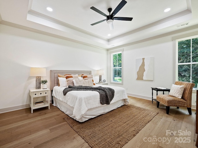 bedroom featuring a raised ceiling, visible vents, light wood-style flooring, and baseboards