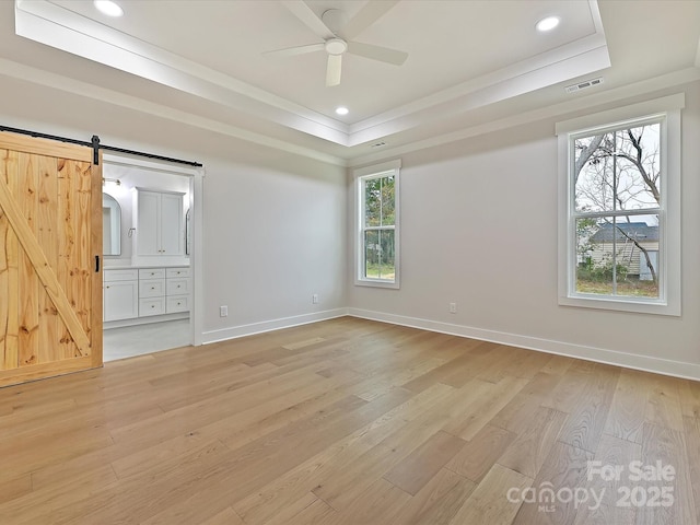 unfurnished bedroom featuring a raised ceiling, visible vents, light wood-style flooring, a barn door, and baseboards