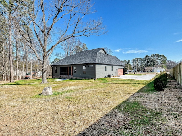 view of home's exterior featuring a shingled roof, concrete driveway, a yard, and fence