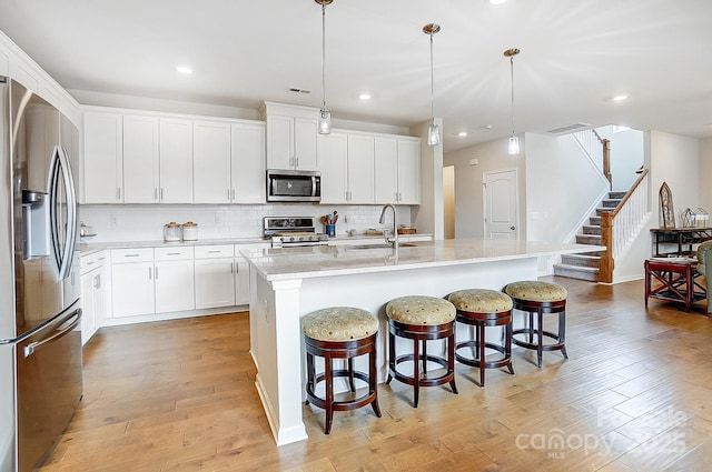 kitchen with a sink, decorative backsplash, appliances with stainless steel finishes, and light wood finished floors