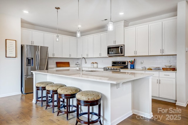 kitchen with wood finished floors, a sink, appliances with stainless steel finishes, a kitchen bar, and backsplash