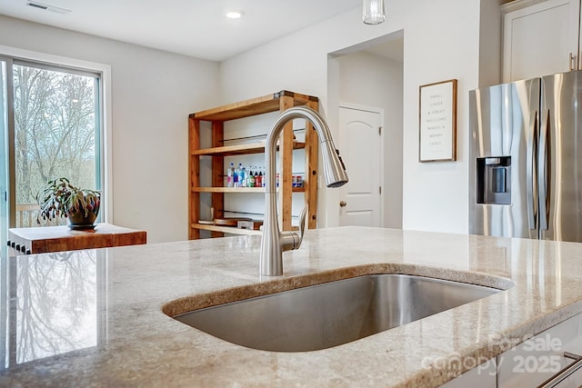 kitchen with light stone countertops, visible vents, recessed lighting, a sink, and stainless steel refrigerator with ice dispenser