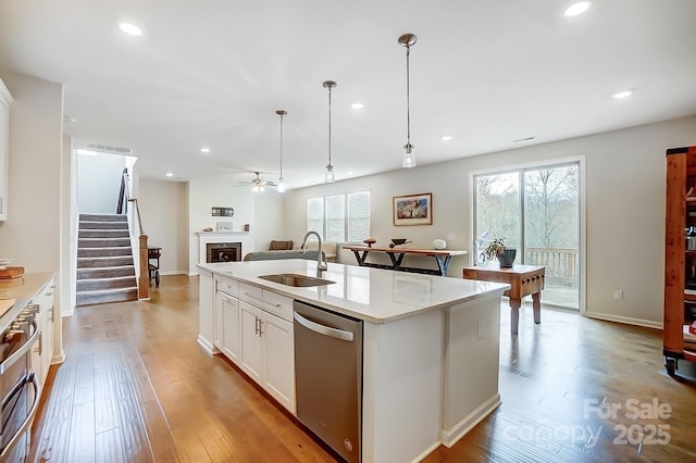 kitchen with a sink, stainless steel dishwasher, open floor plan, light wood-style floors, and a fireplace