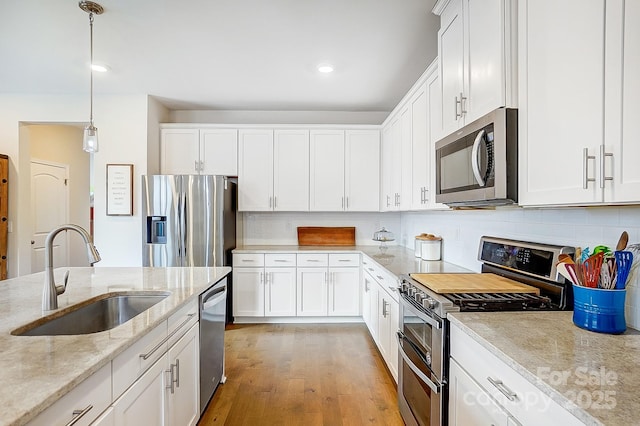 kitchen featuring white cabinets, stainless steel appliances, light wood-style flooring, and a sink