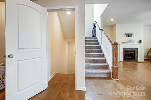 stairway with a fireplace, recessed lighting, wood finished floors, and baseboards