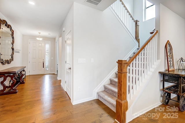 foyer with stairway, wood finished floors, visible vents, and baseboards