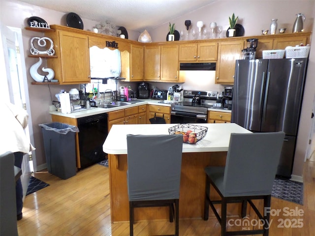 kitchen featuring light wood-style flooring, under cabinet range hood, stainless steel appliances, vaulted ceiling, and light countertops