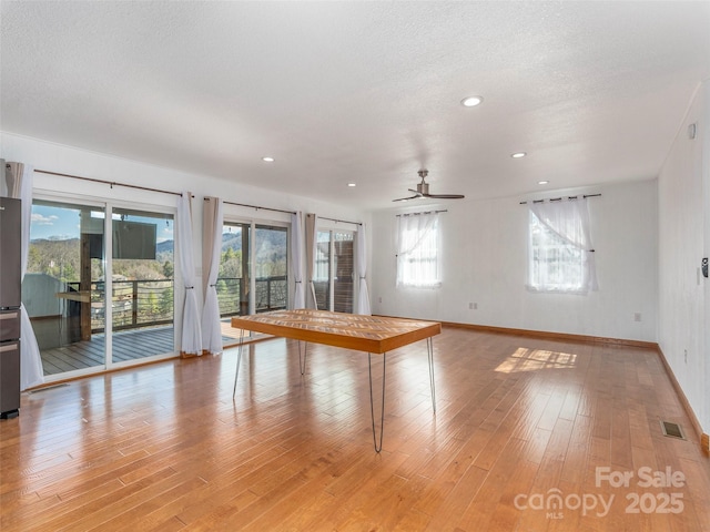 empty room featuring baseboards, visible vents, light wood-style flooring, ceiling fan, and a textured ceiling