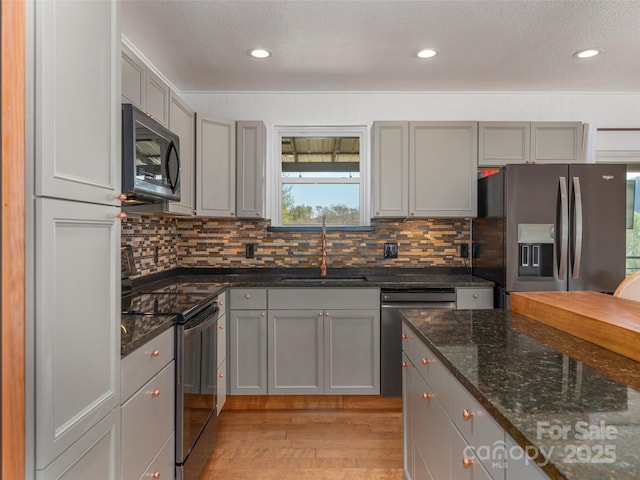 kitchen with appliances with stainless steel finishes, gray cabinetry, a sink, and light wood finished floors