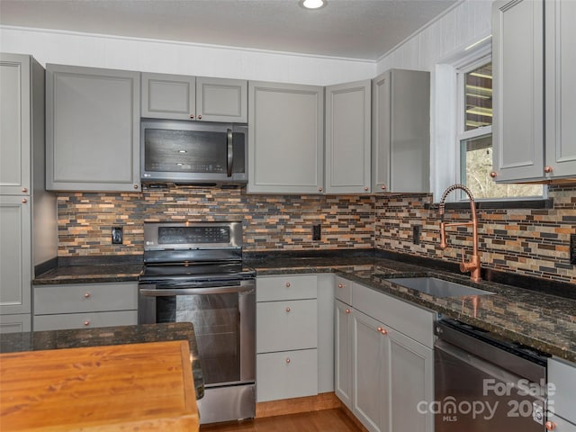 kitchen with decorative backsplash, stainless steel appliances, a sink, and gray cabinetry