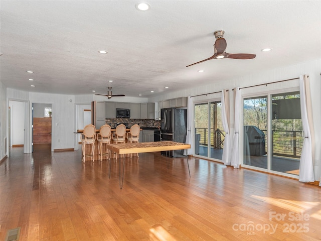 living room with light wood-type flooring, ceiling fan, a textured ceiling, and recessed lighting