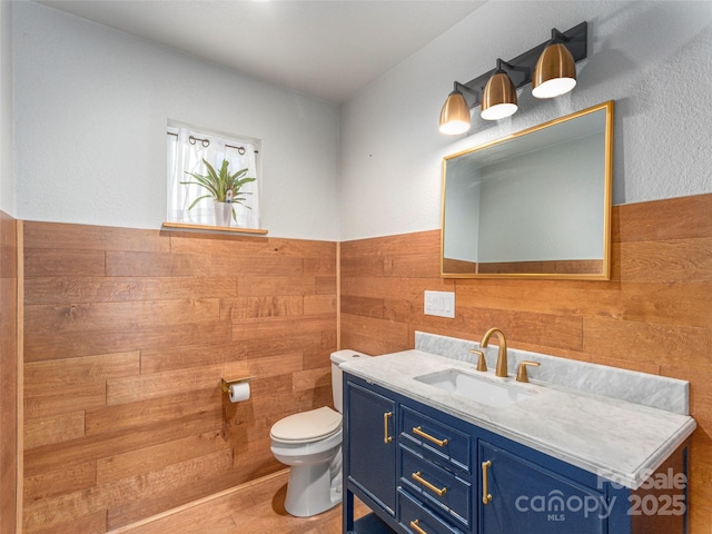 half bathroom featuring wood walls, wainscoting, vanity, and toilet