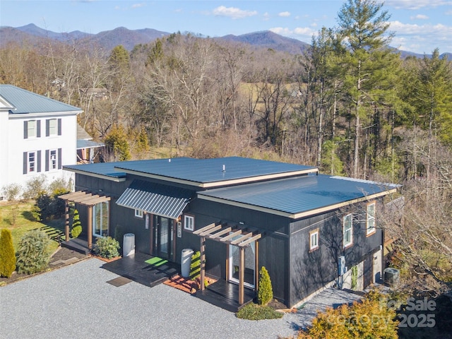 view of front of house with metal roof, driveway, a forest view, and a mountain view