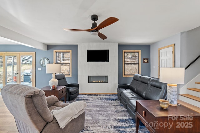 living area featuring a fireplace, stairway, and a ceiling fan