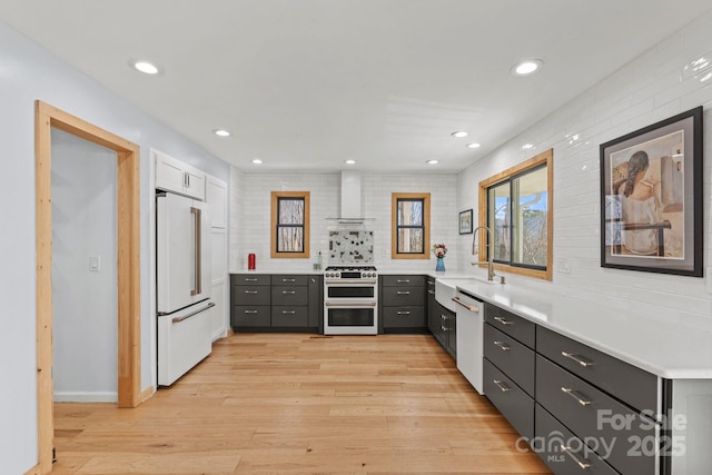 kitchen with a sink, light countertops, wall chimney range hood, light wood finished floors, and high end appliances