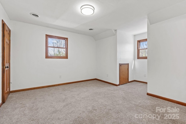 carpeted spare room with visible vents, vaulted ceiling, and baseboards