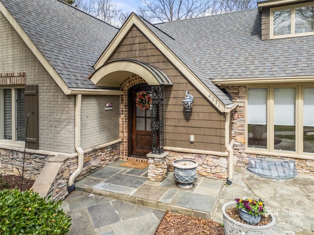 view of exterior entry featuring stone siding, brick siding, and roof with shingles