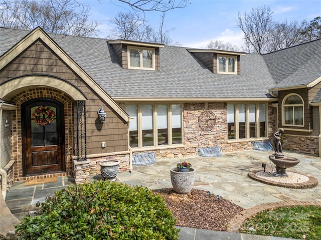 entrance to property with a shingled roof, stone siding, and a patio