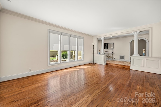 unfurnished living room with decorative columns, wood-type flooring, visible vents, ornamental molding, and baseboards