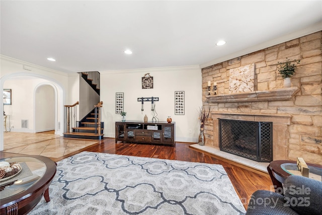 living area featuring arched walkways, wood finished floors, a fireplace, and stairs