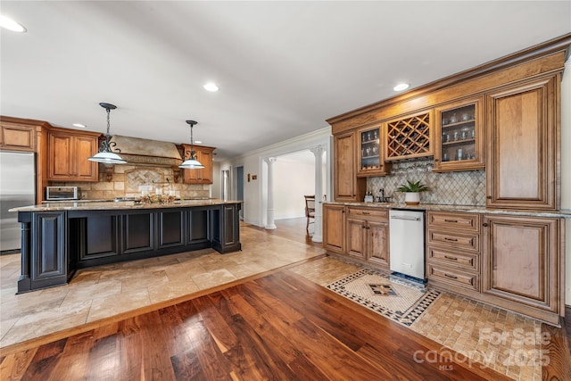 kitchen with decorative backsplash, appliances with stainless steel finishes, brown cabinetry, light wood-style floors, and premium range hood