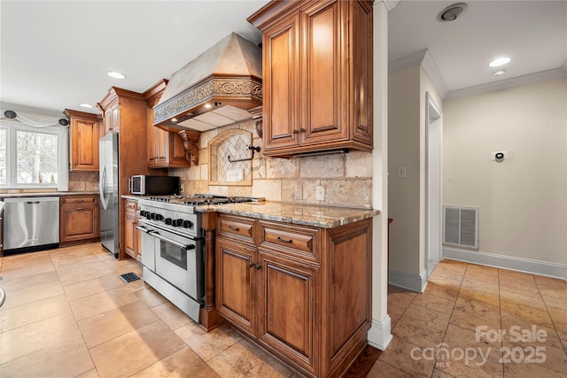 kitchen featuring visible vents, brown cabinetry, custom range hood, light stone countertops, and stainless steel appliances