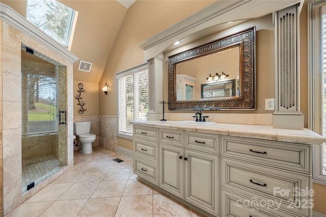 full bathroom featuring vaulted ceiling with skylight, toilet, visible vents, vanity, and a stall shower