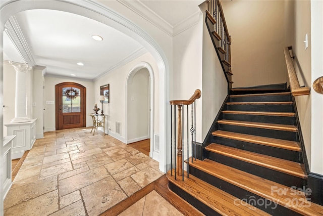 foyer entrance featuring stone tile floors, decorative columns, baseboards, arched walkways, and crown molding