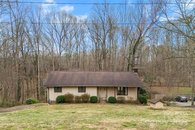 ranch-style house featuring roof with shingles, a wooded view, a chimney, and a front lawn