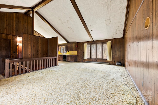 unfurnished living room with vaulted ceiling with beams, carpet floors, baseboard heating, and wooden walls