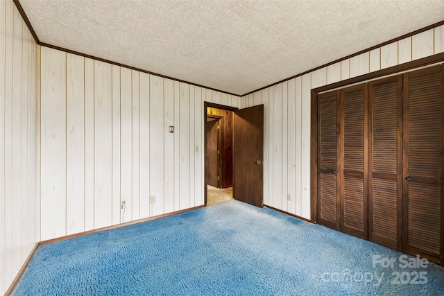 unfurnished bedroom featuring carpet, a closet, ornamental molding, a textured ceiling, and baseboards