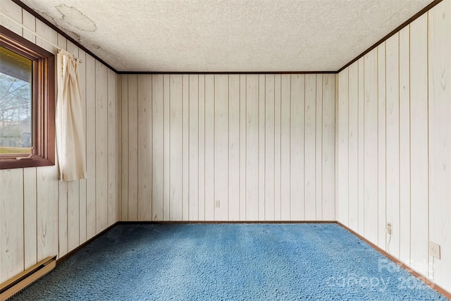 carpeted spare room with a textured ceiling, ornamental molding, a baseboard radiator, and wooden walls