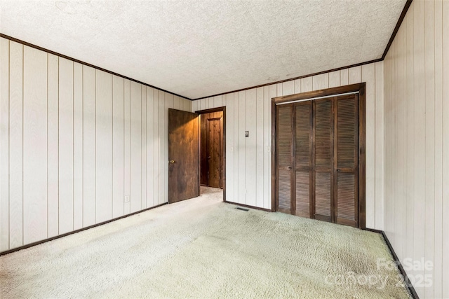 unfurnished bedroom with crown molding, a closet, visible vents, carpet flooring, and a textured ceiling