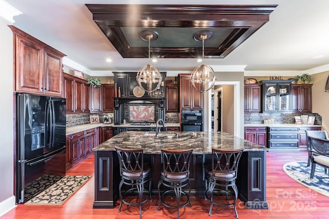 kitchen with an island with sink, black appliances, crown molding, and a sink