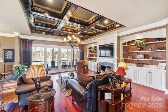 living room with coffered ceiling, wood finished floors, crown molding, a fireplace, and a notable chandelier