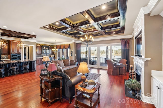 living room featuring a chandelier, dark wood-type flooring, a fireplace, coffered ceiling, and ornamental molding