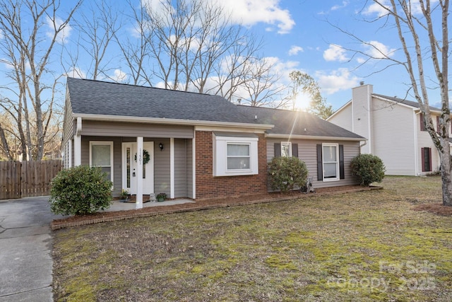 view of front facade featuring brick siding, fence, a front lawn, and roof with shingles