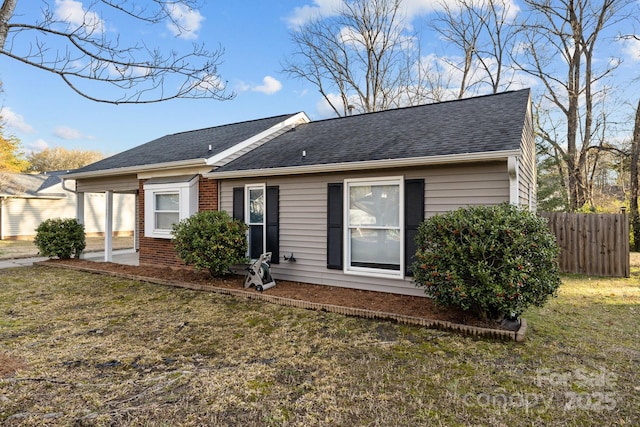 rear view of property with a shingled roof, brick siding, fence, and a lawn