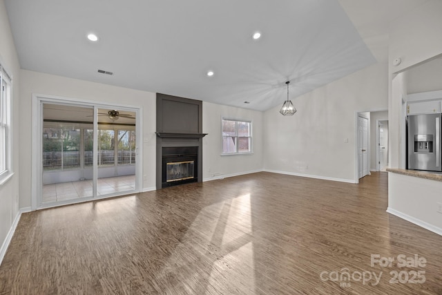 unfurnished living room featuring lofted ceiling, recessed lighting, a large fireplace, wood finished floors, and baseboards